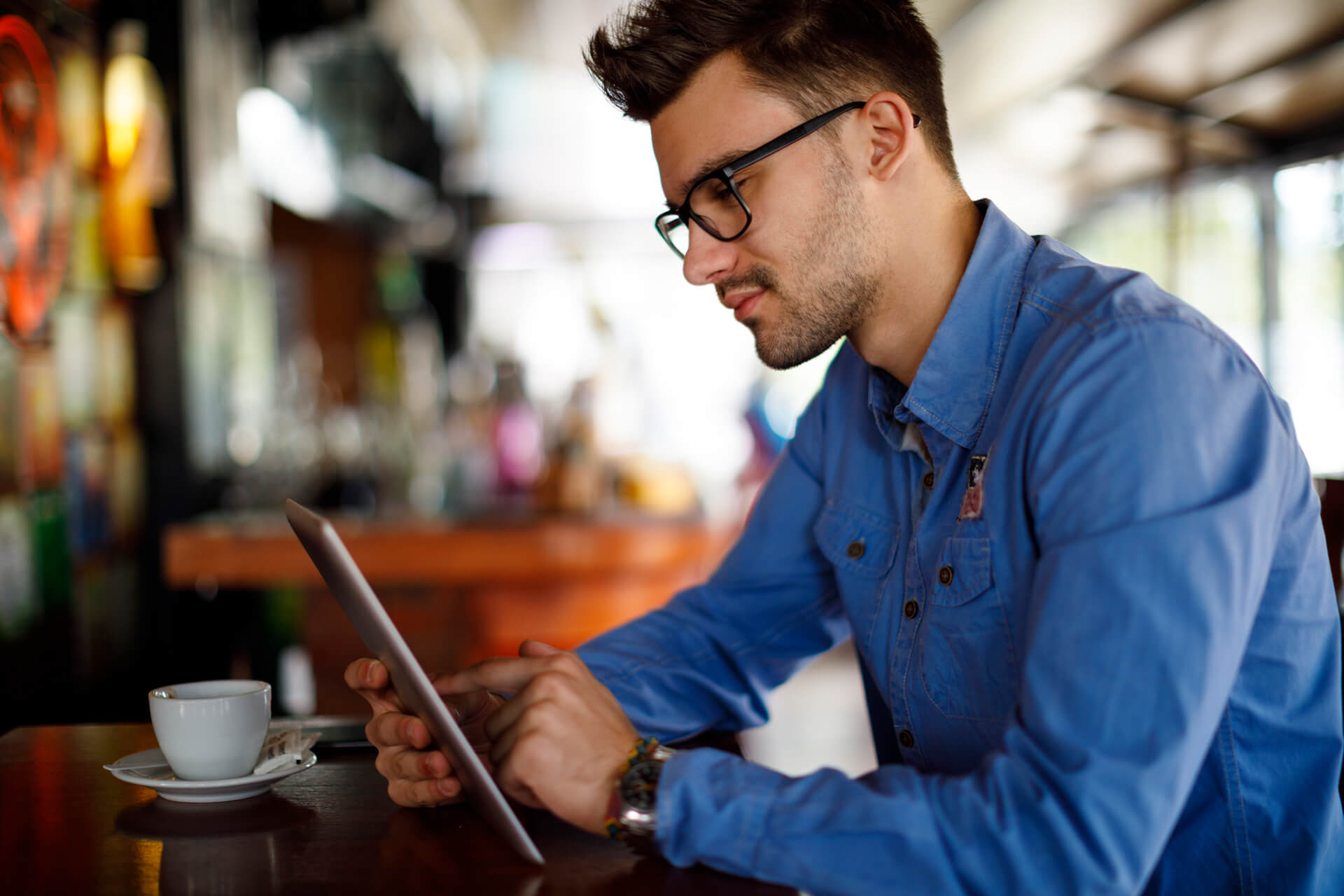 Junger Mann liest etwas im Tablet in einem Café