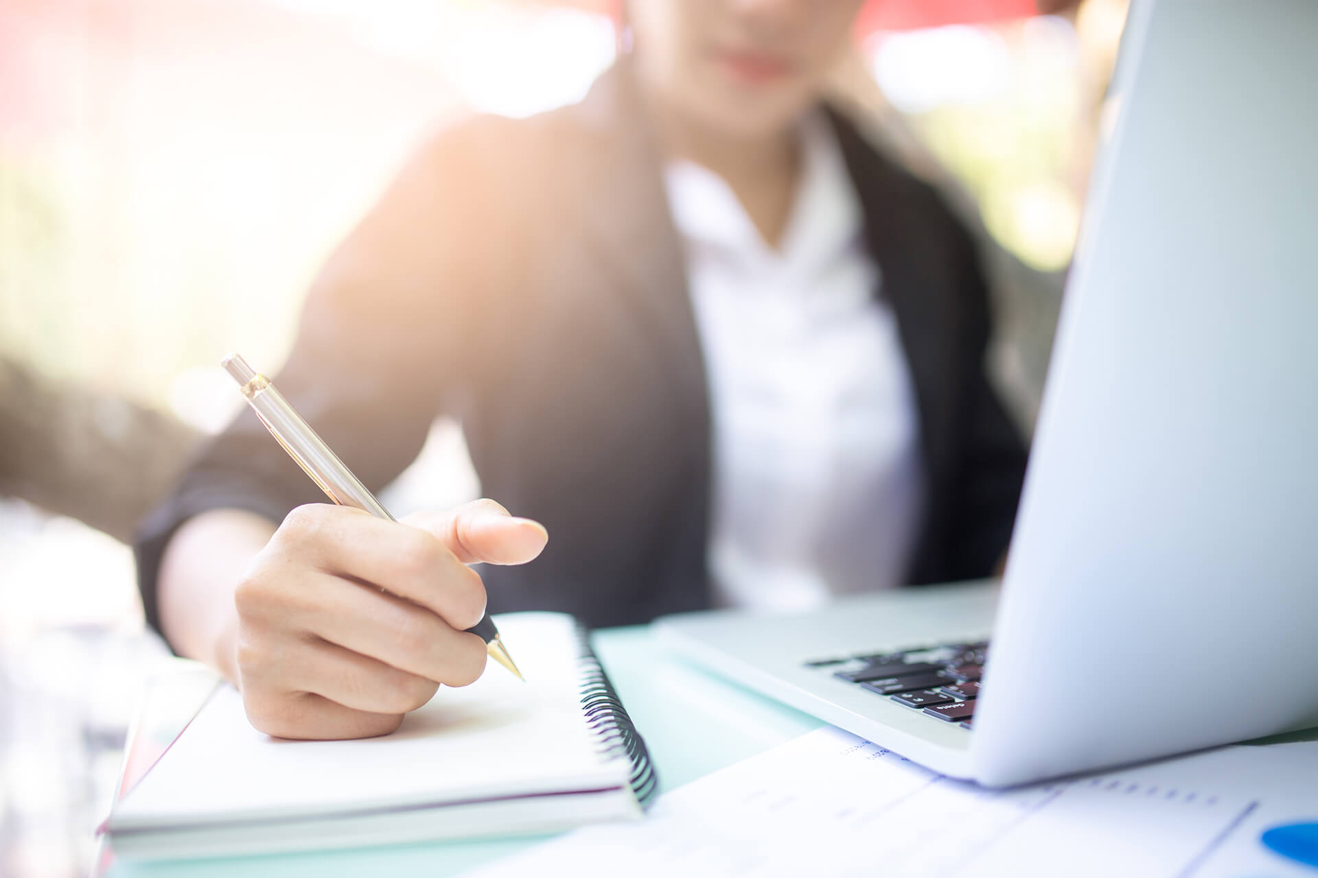 Frau sitzt am Schreibtisch und macht sich neben Laptop Notizen