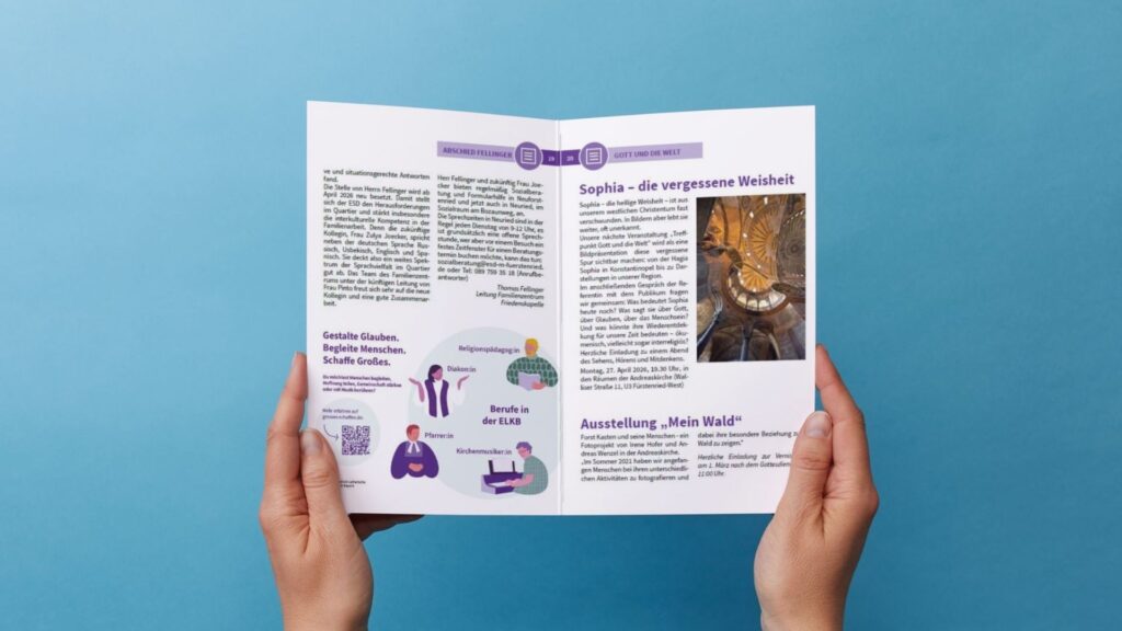 Eine Person hält eine aufgeschlagene Broschüre mit deutschem Text, violetten Grafiken und dem Foto einer Statue in einem Gebäude vor einem einfarbigen blauen Hintergrund in der Hand.