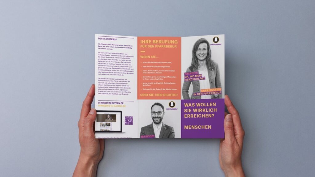 Eine Person, die eine aufgeschlagene Broschüre mit deutschem Text, dem Foto einer Frau sowie violetten, orangefarbenen und weißen Bereichen auf grauem Hintergrund in der Hand hält.