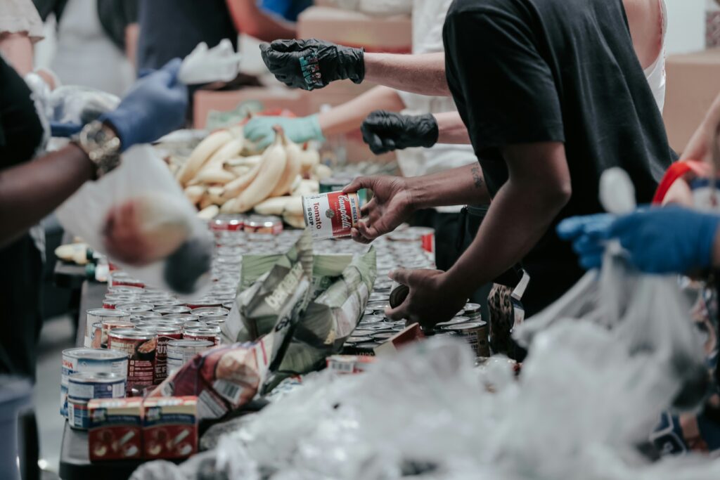 Menschen mit Handschuhen sortieren und verteilen Konserven, Bananen und andere Lebensmittel in einer Tafel oder bei einer Hilfsaktion für die Gemeinde.