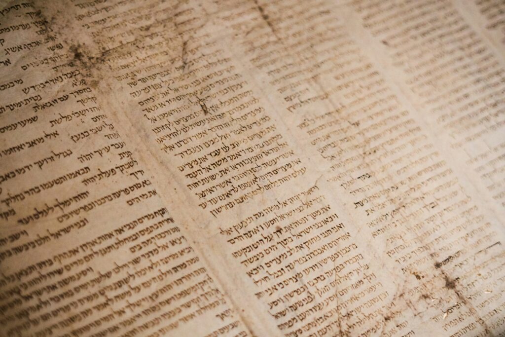Eine Nahaufnahme eines gealterten, fleckigen Manuskripts in hebräischer Schrift mit erkennbaren Textspalten und dunklen Flecken auf dem Pergament.